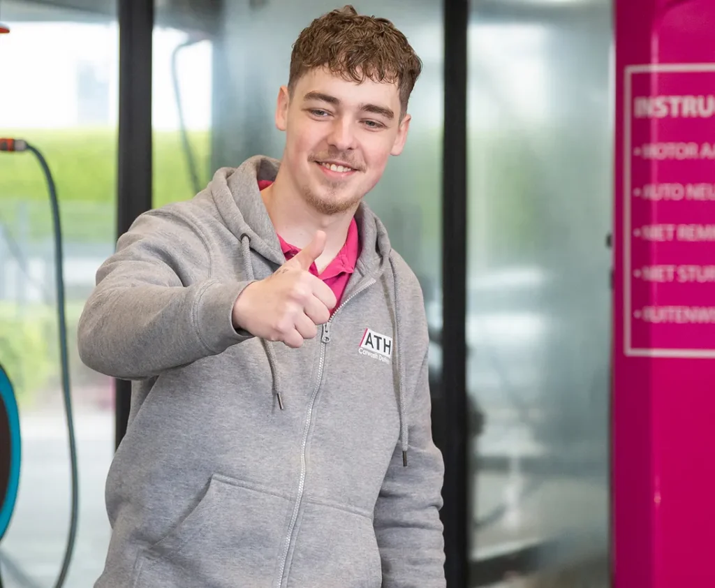 Een jonge man in een grijze hoodie steekt zijn duim omhoog en glimlacht.