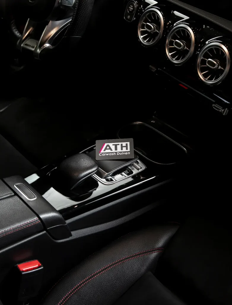 Close-up van het luxe dashboard en middenconsole van een auto, met een kaartje van ATH Carwash Duiven.