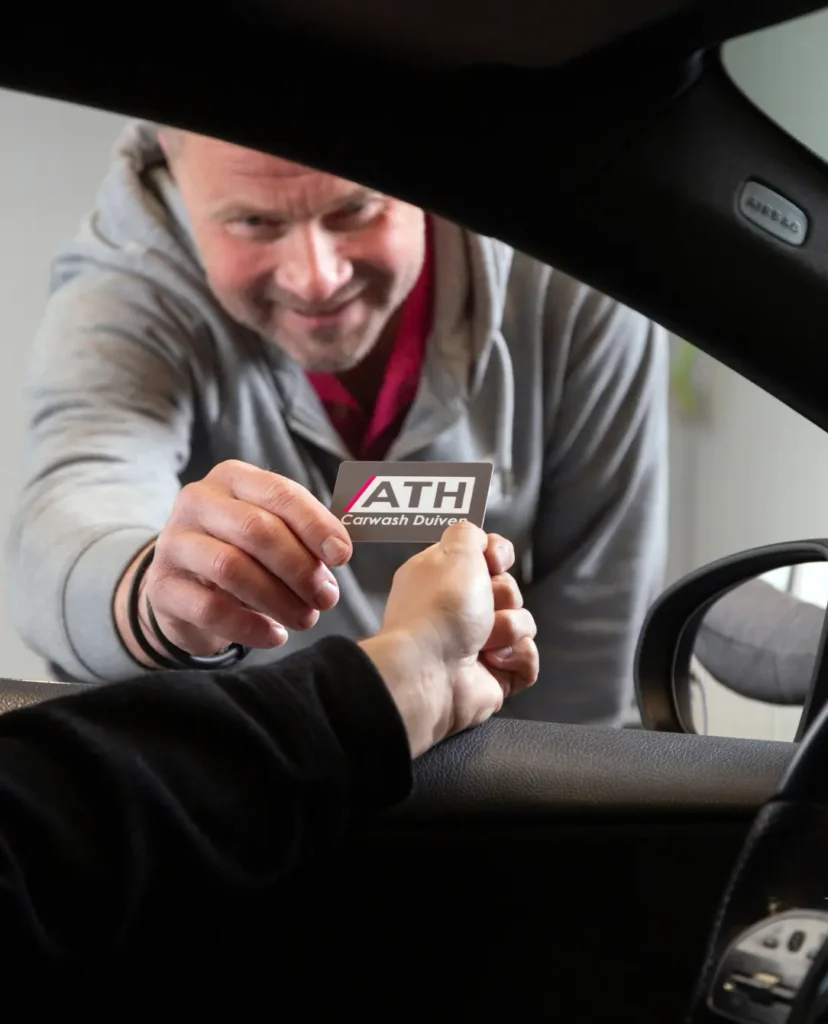 Een man geeft een ATH Carwash Duiven kaart aan een persoon in een auto.